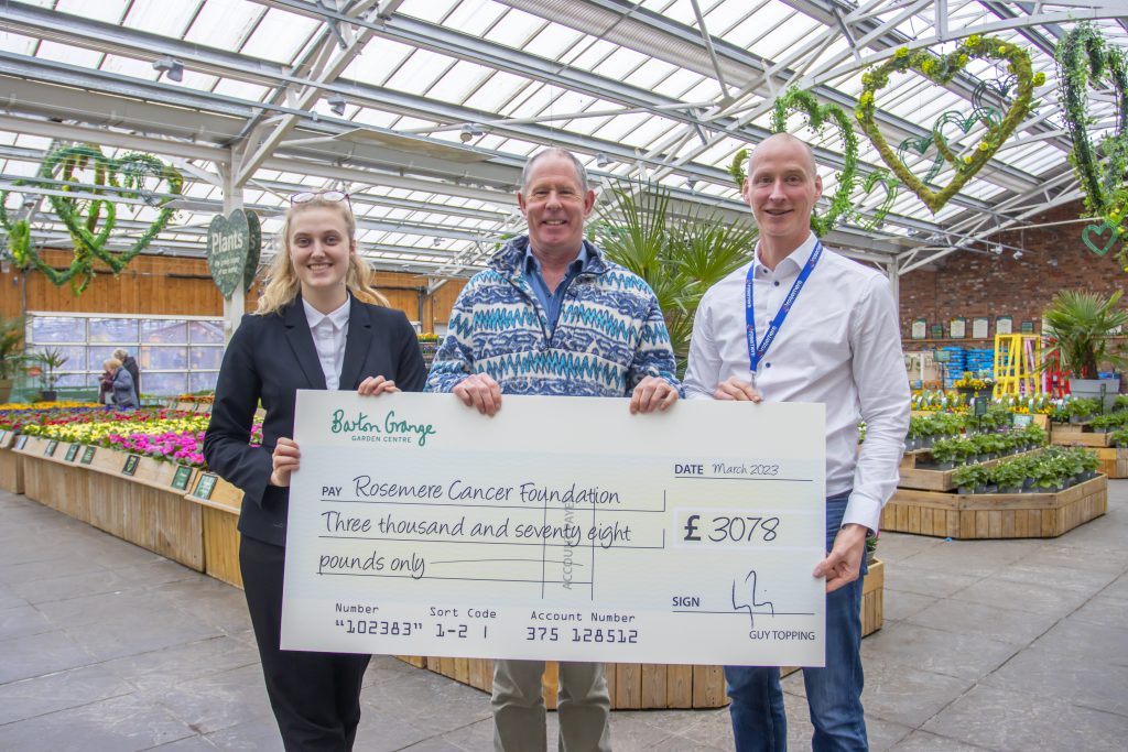 Image of three people holding large cheque in greenhouse