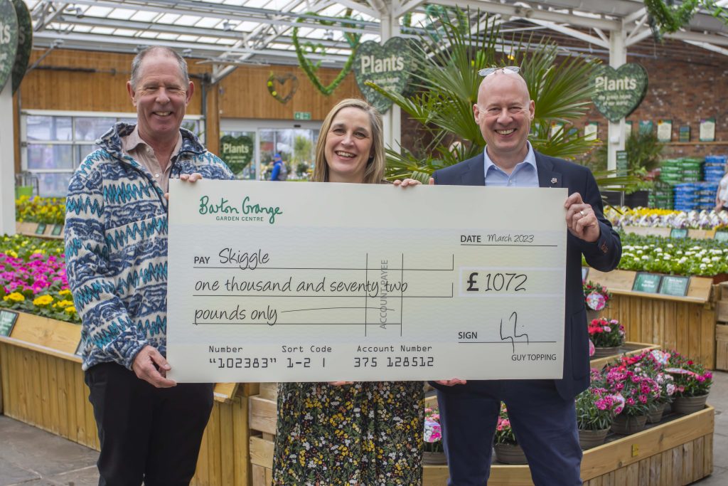 Image of three people holding large cheque in greenhouse