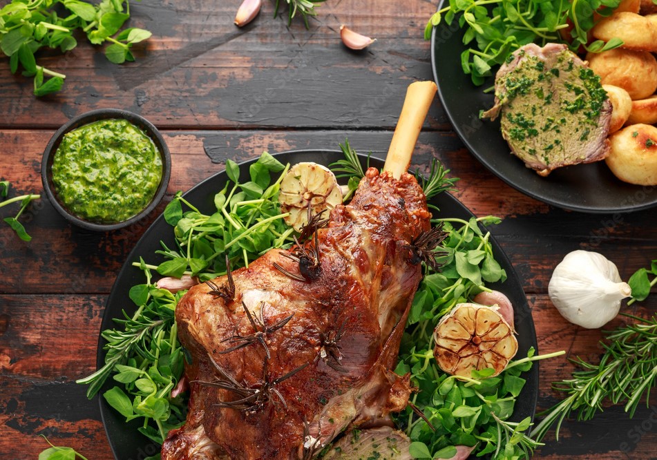 Image of barbecued lamb leg on a plate surrounded with herbs and salad leaves