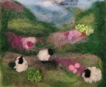 Felt landscape with rolling hills, blue sky, pink flowers and fluffy sheep.